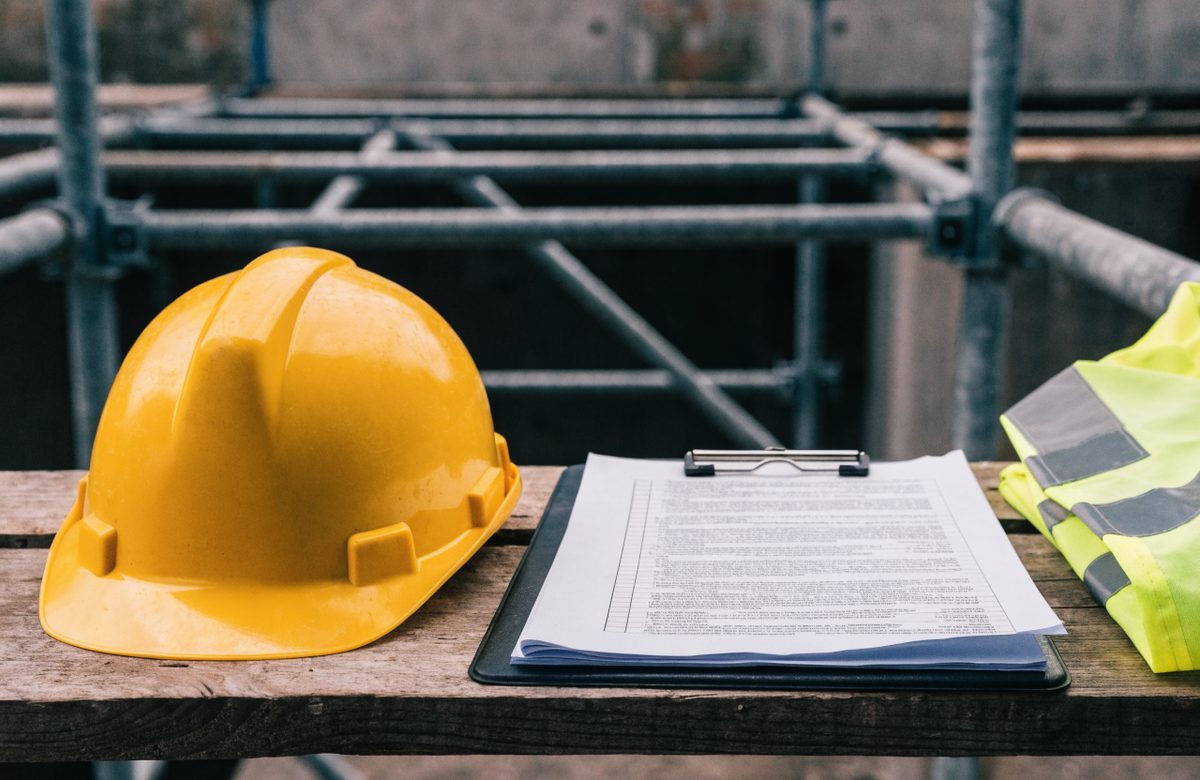 A hard hat, hi-vis vest and a risk assessment on a clipboard resting on scaffold boards at a work site